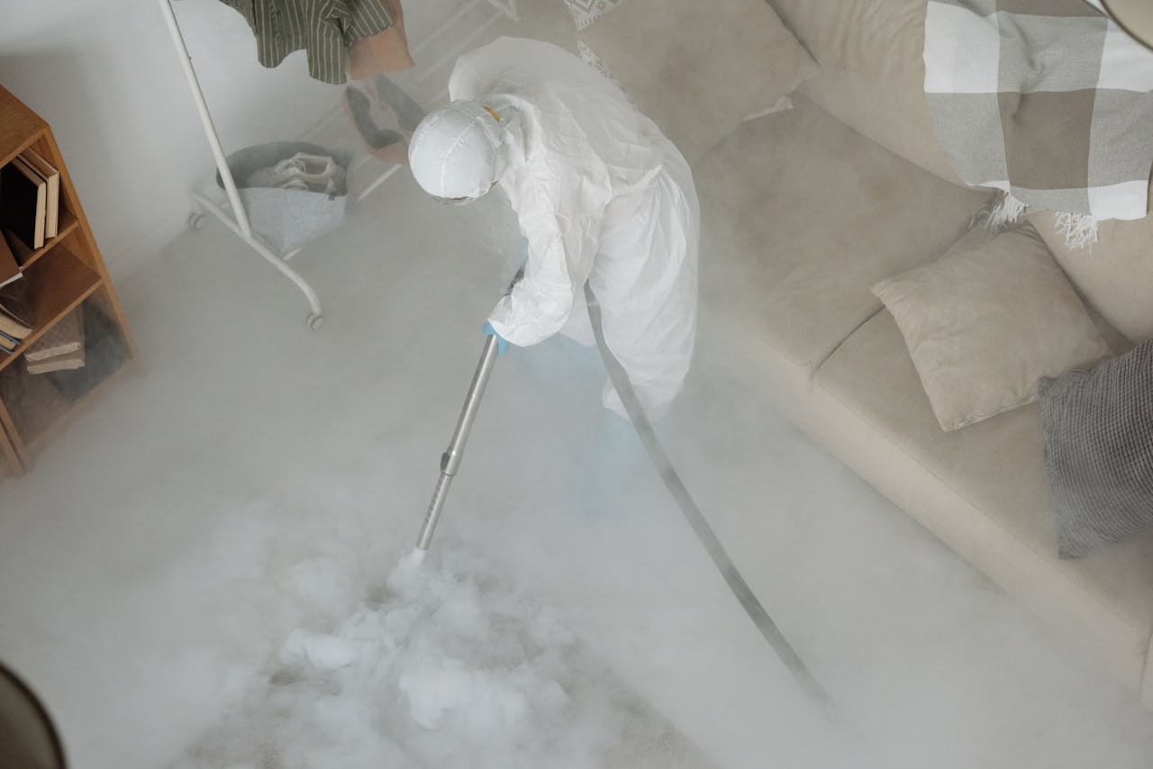 A person in protective gear disinfects a living room using a fogging machine for sanitation.